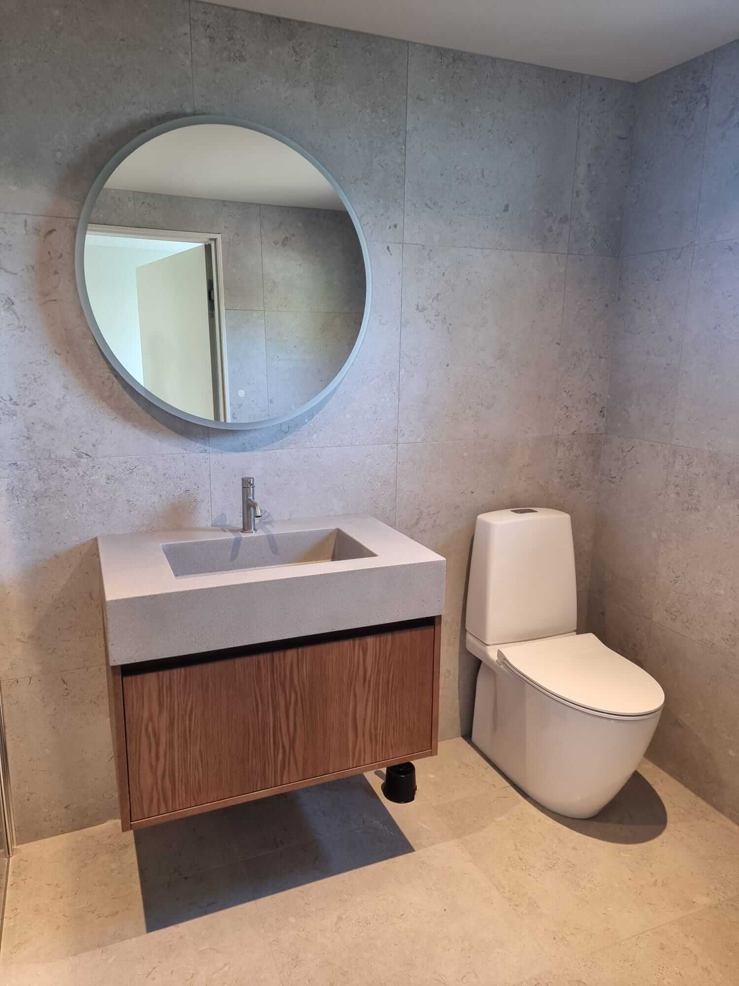 Bathroom with round mirror, toilet and floating vanity with wooden cabinet.