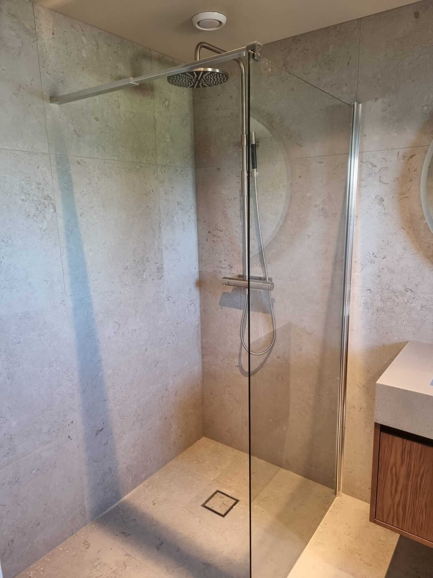 Modern shower with glass wall and rain showerhead in beige bathroom.