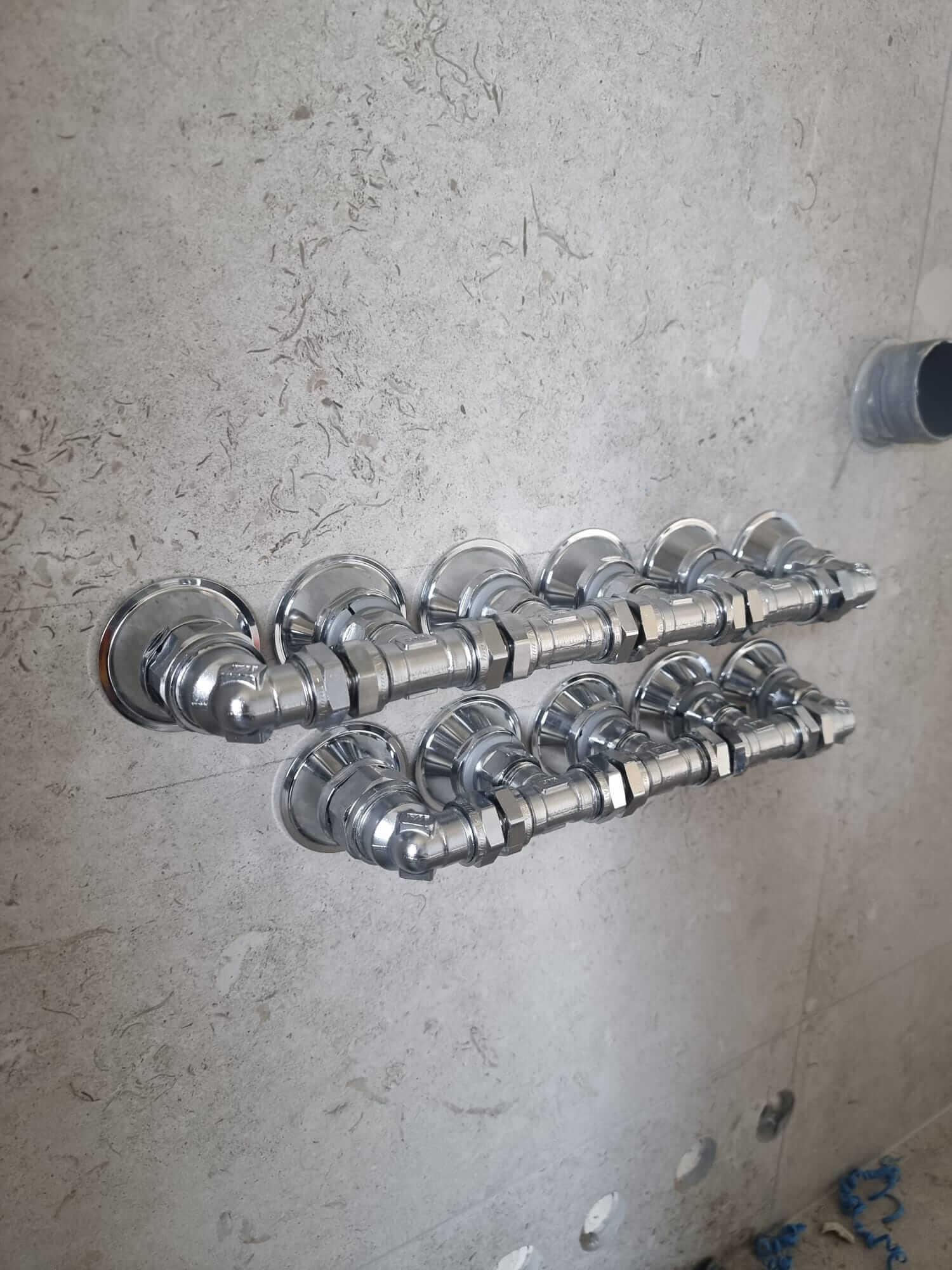 Chrome pipe manifolds mounted on wall with grey stone tiles