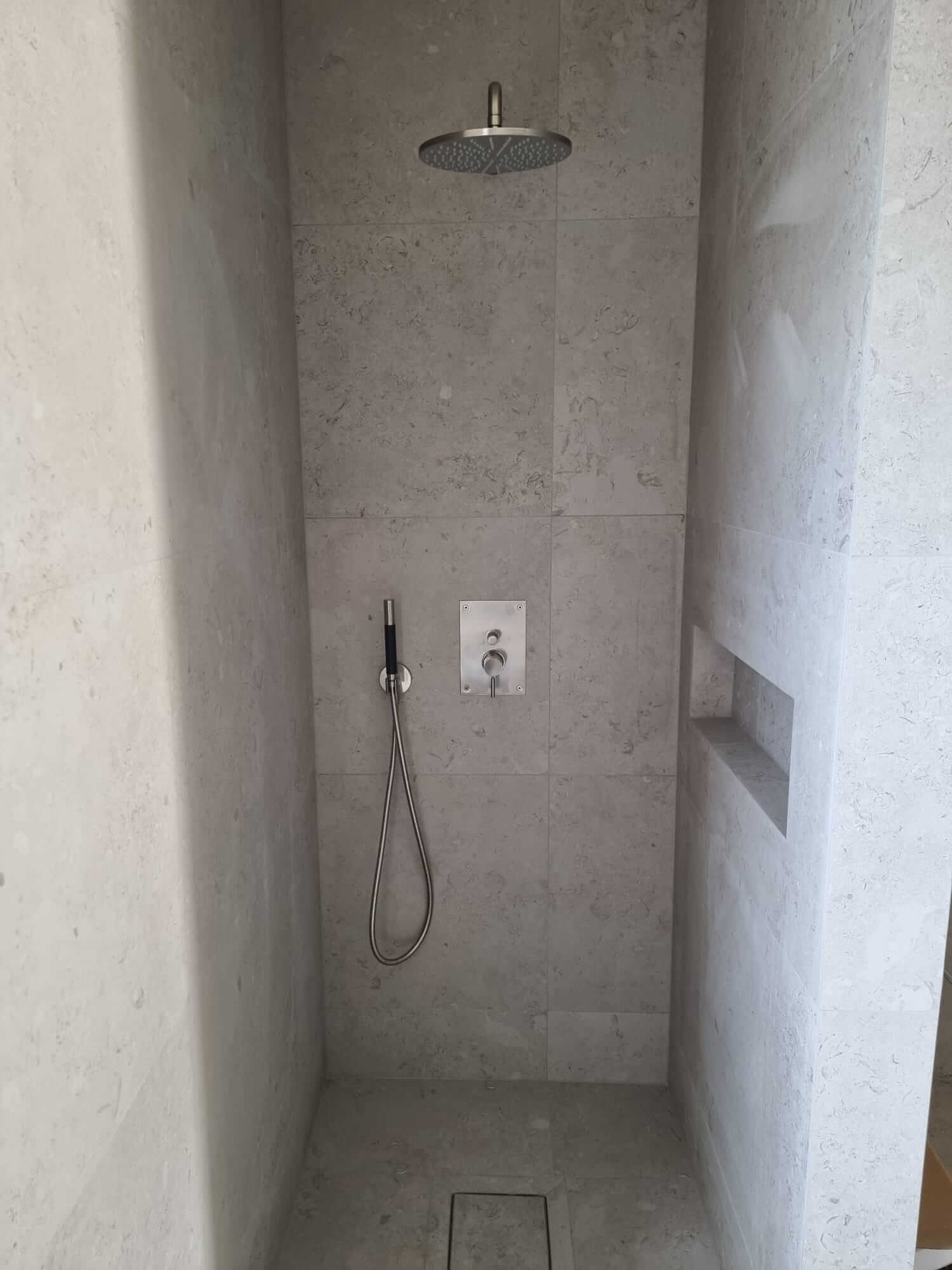 Stylish shower corner with rain shower and handheld shower in beige stone tiles.