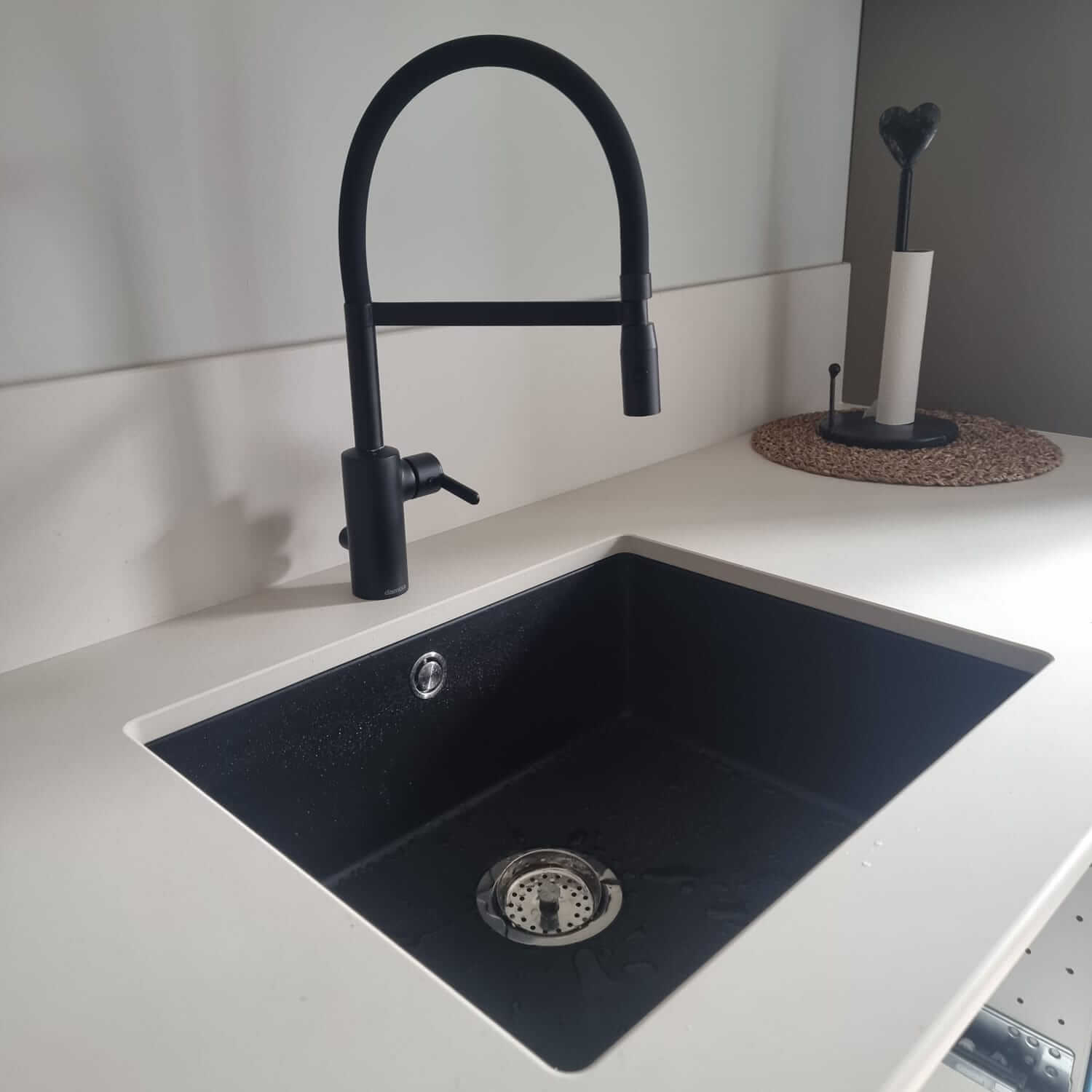 Modern black kitchen faucet with black sink in white countertop.